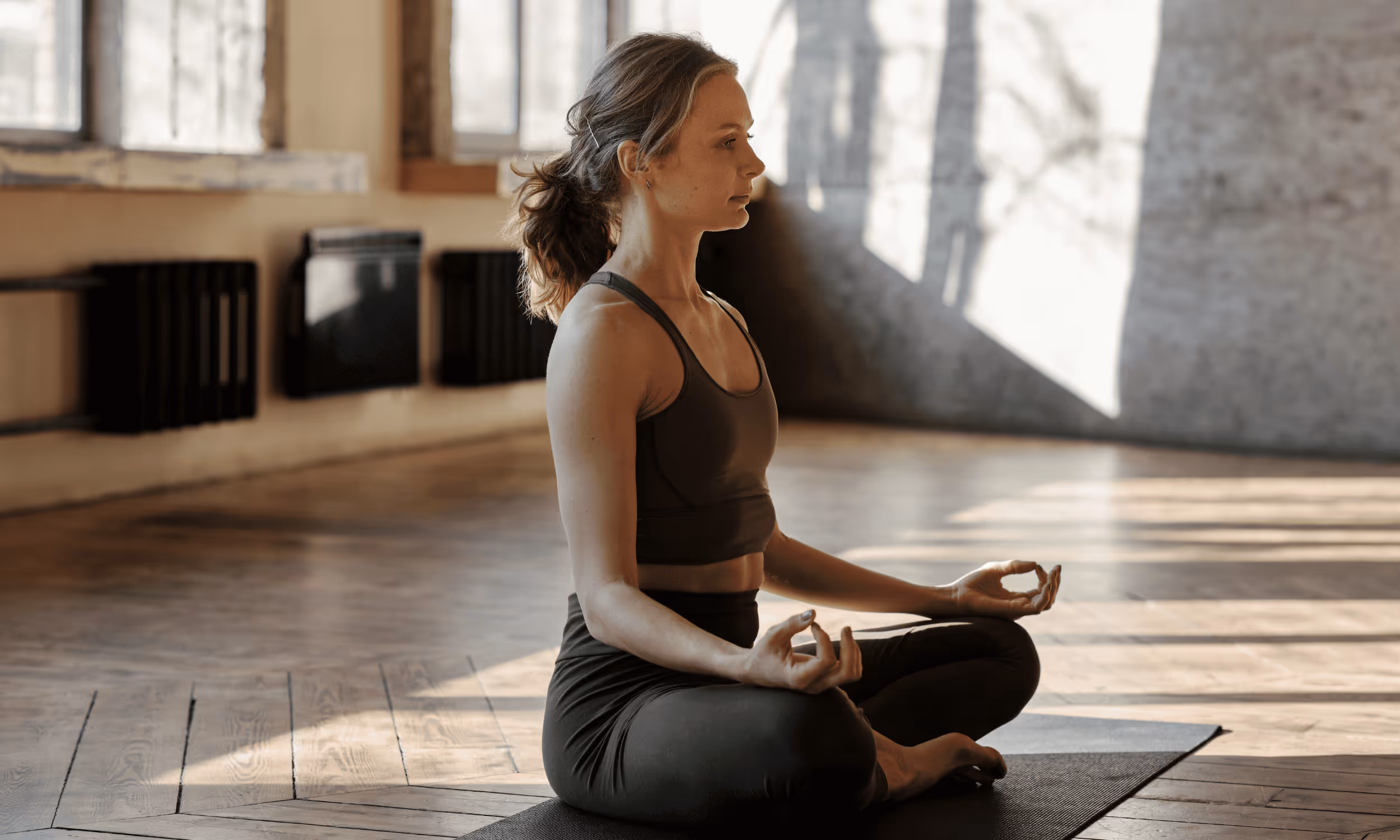 Frau sitzt im Schneidersitz auf einer Yogamatte.