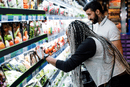 Zwei Personen vergleichen Produkte vor einem Supermarktregal.