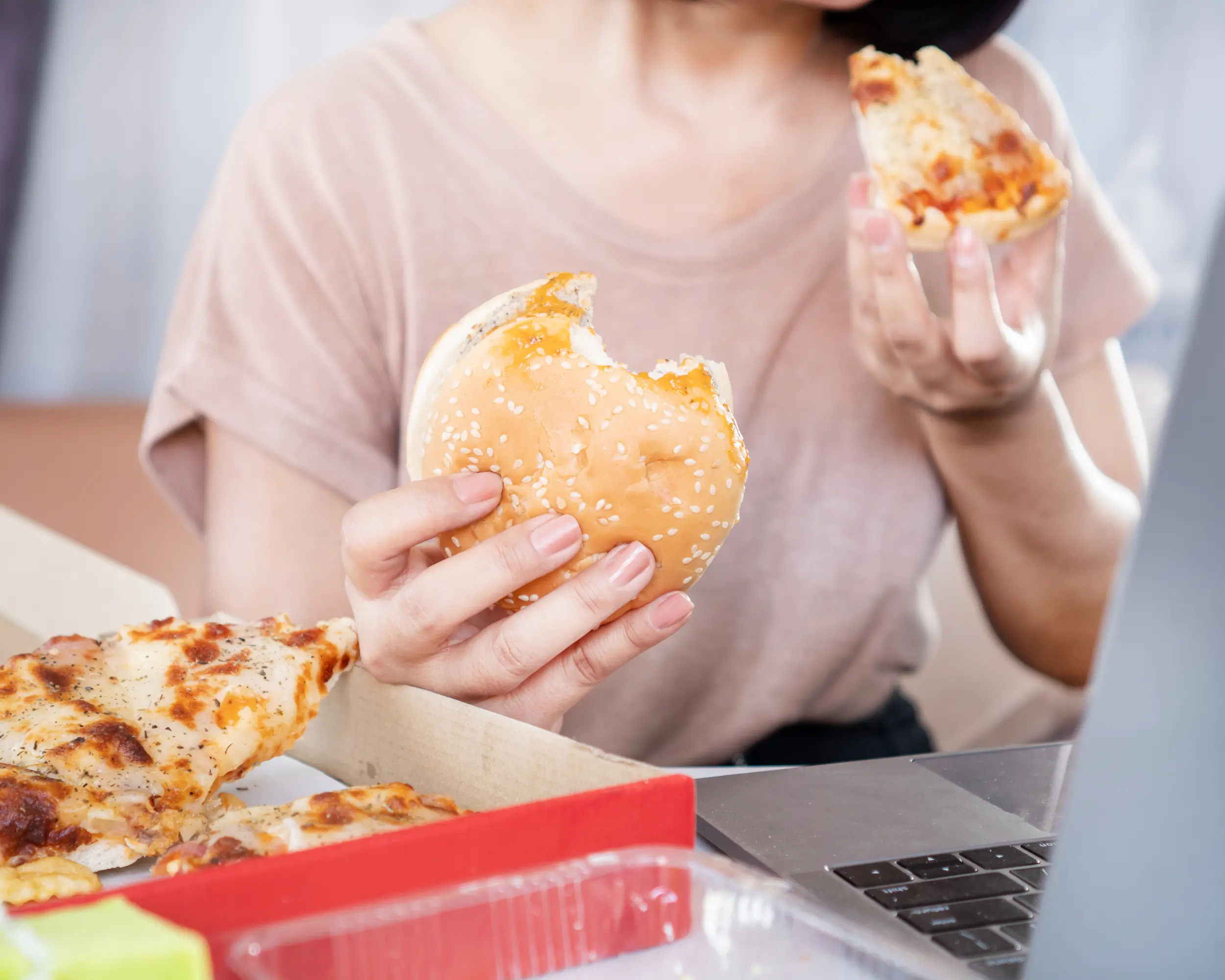 Person hält einen Burger und ein Stück Pizza.