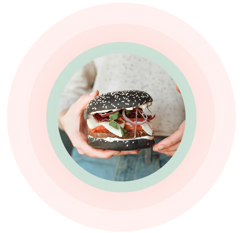Person mit einem Gourmet-Burger mit schwarzem Sesambrötchen, Salat, Tomate, Zwiebel und Sauce.