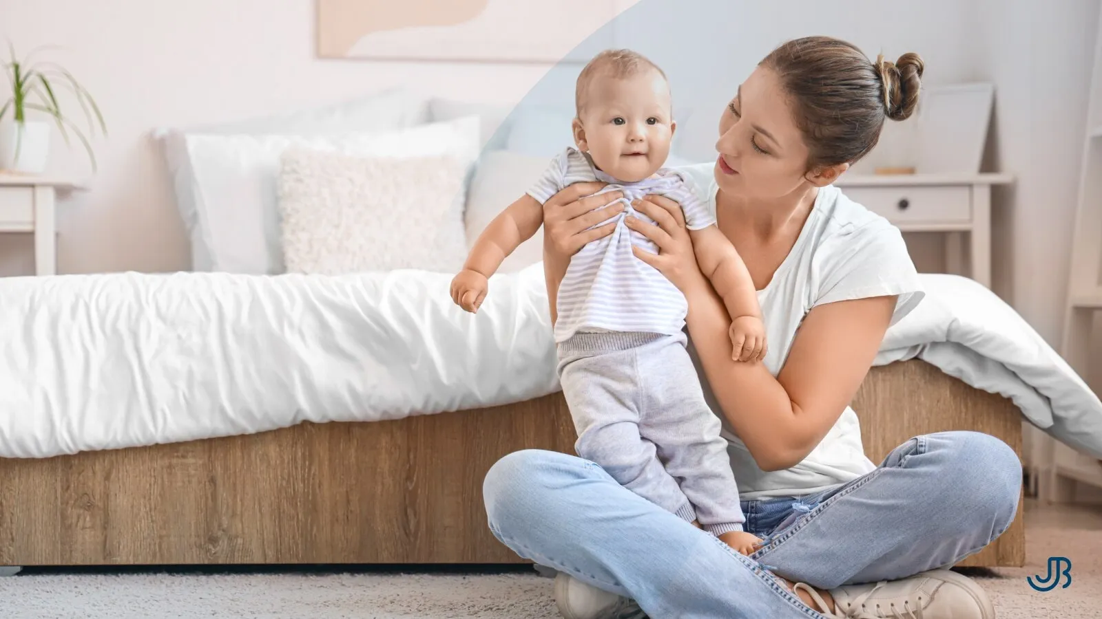 Junge Mutter sitzt mit ihrem Baby im Schlafzimmer auf dem Boden, zeigt Zuneigung und kümmert sich liebevoll um das Kind. Jan Bahmann gibt Fitness-Tipps für Mütter.