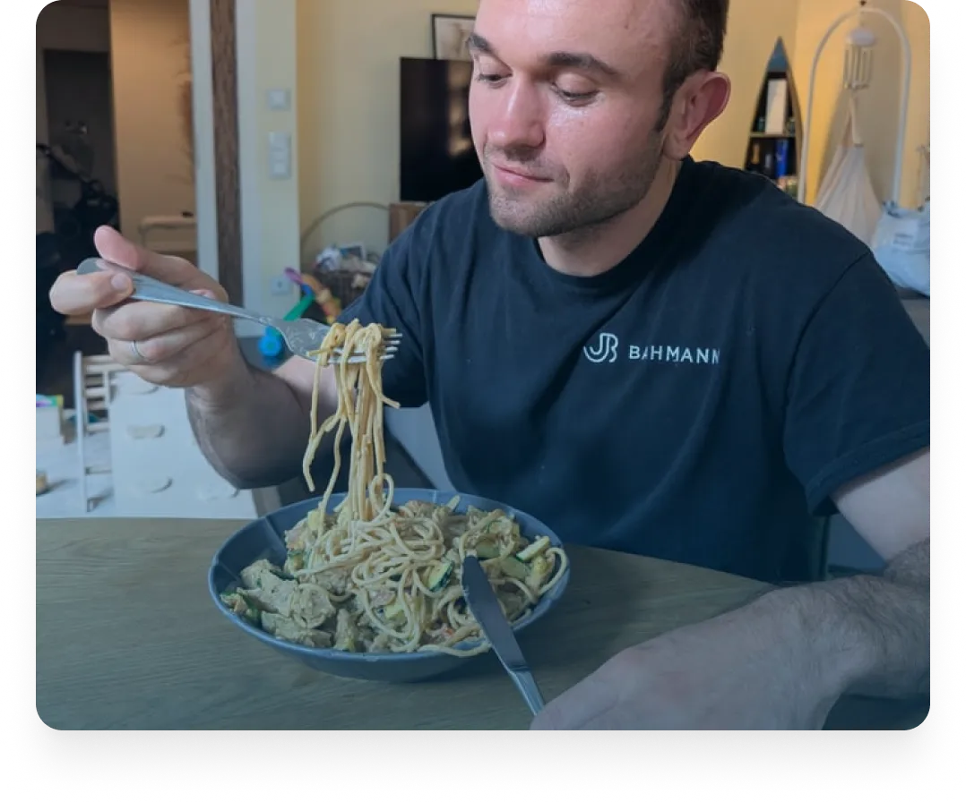Mann in einem schwarzen Hemd, der Spaghetti mit einer Gabel über einer Schüssel Pasta auf einem Holztisch herumwirbelt.